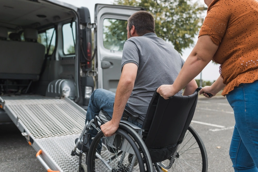 Support worker pushing disabled man into van